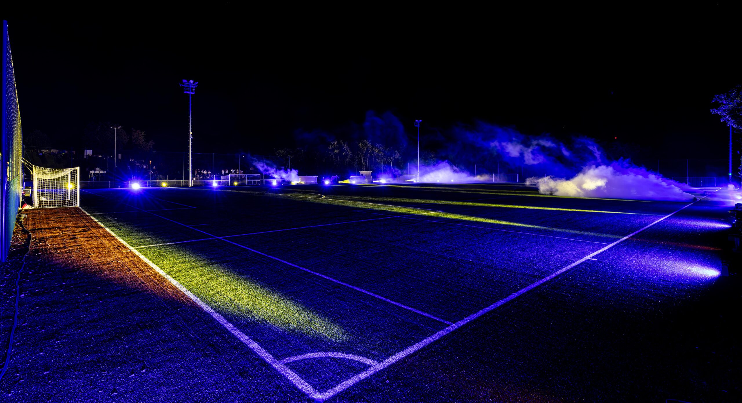 Terrain de football illuminé par des lumières violettes en pleine nuit.